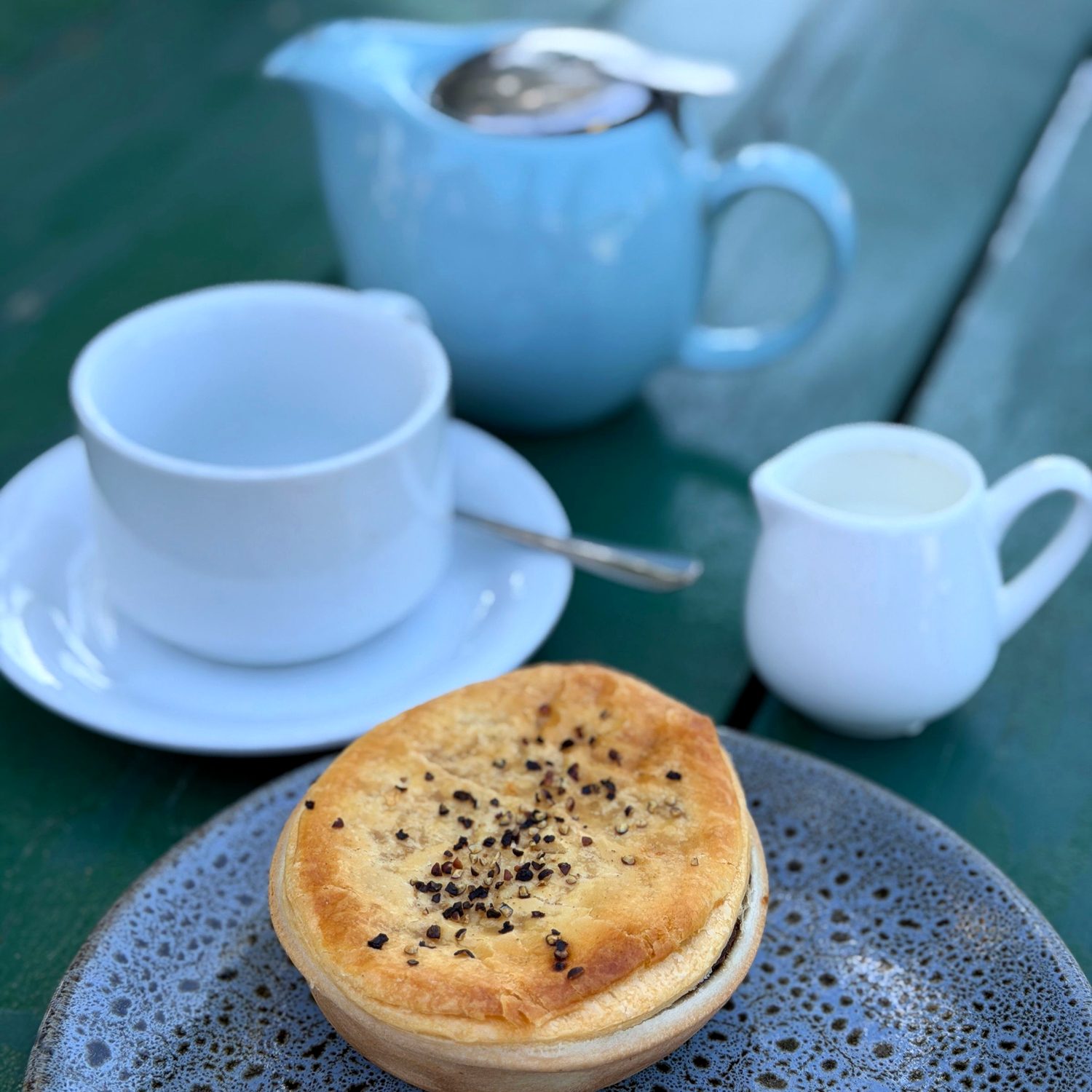 A golden, flaky Australian meat pie served with a pot of tea