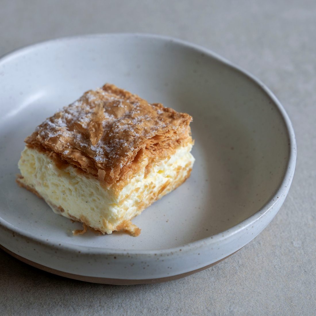 A slice of vanilla custard slice with a flaky pastry top, dusted with icing sugar
