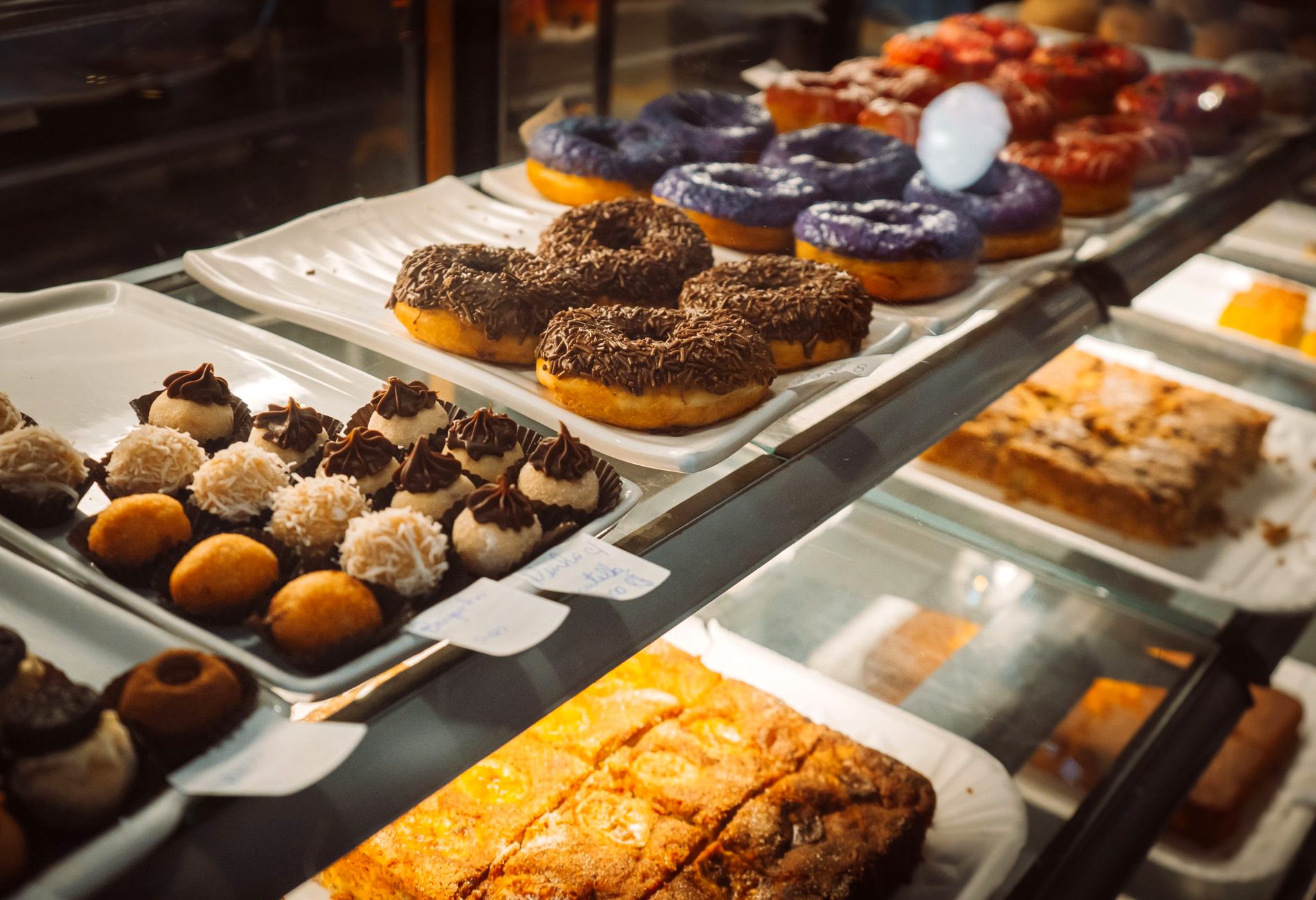 A warm bakery display case filled with glazed doughnuts, chocolate treats and fresh cakes